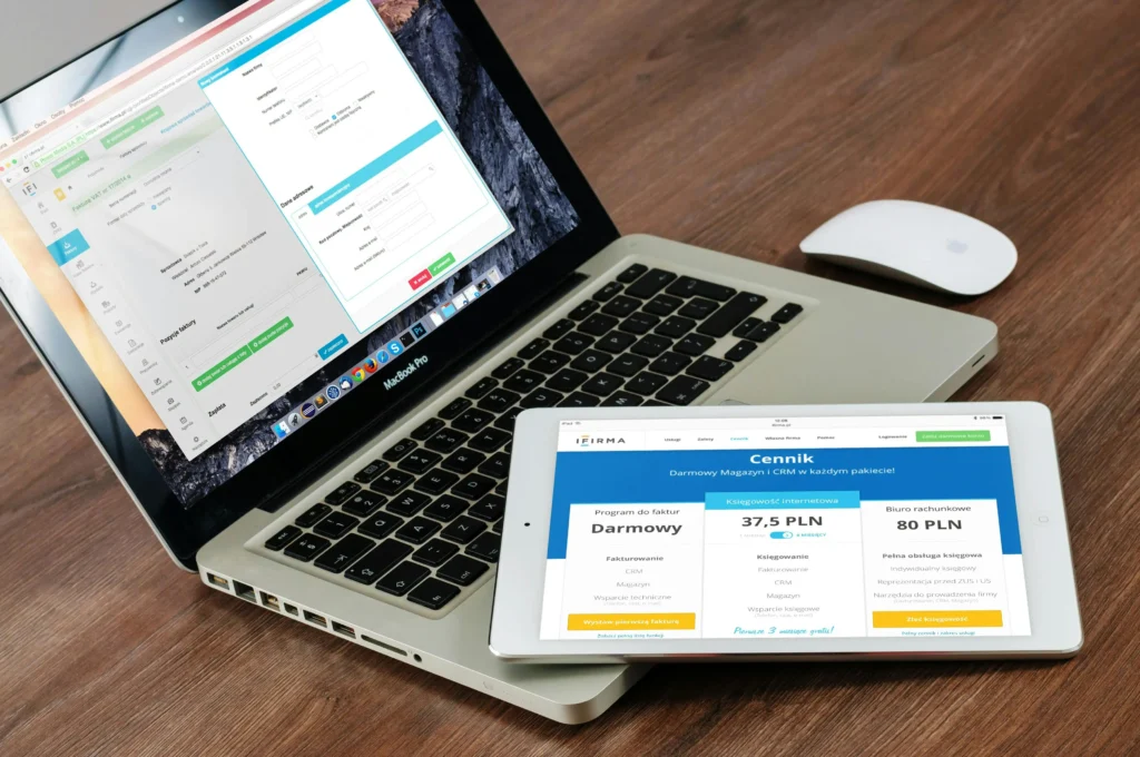Laptop and tablet displaying business CRM and accounting software dashboards for managing invoices, pricing and online business operations.