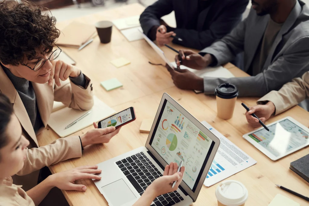Digital marketing team reviewing analytics dashboards and performance reports on laptops, tablets and smartphones during a business strategy meeting.