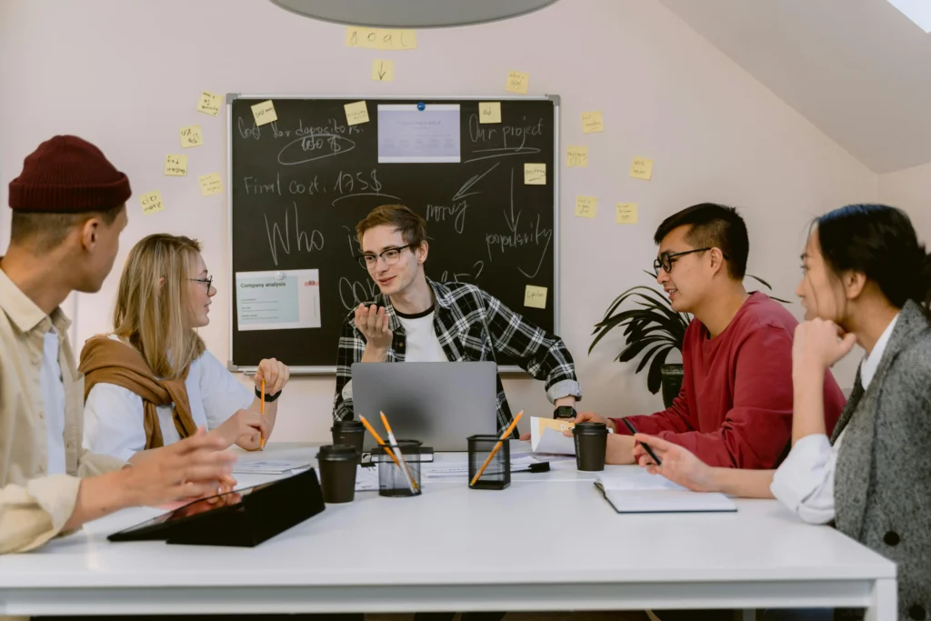 Creative team brainstorming digital marketing strategies and project planning during a collaborative office meeting with laptops, notes and a presentation board.